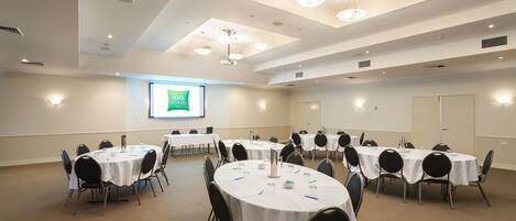 A conference room with multiple round tables, chairs, and a projector screen displaying "Gibbs Styles".