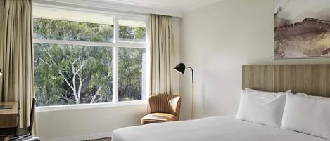 A hotel room with a large bed, a desk, a chair, a suitcase, and a window with curtains.