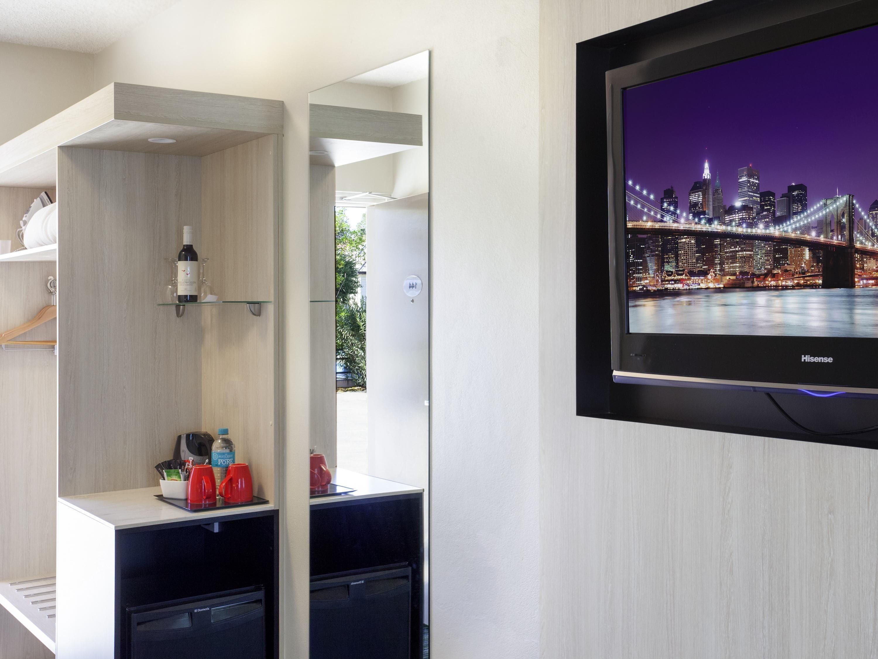 Habitación de hotel con televisor montado que muestra un paisaje urbano, una minibar y un pequeño espacio para sentarse.