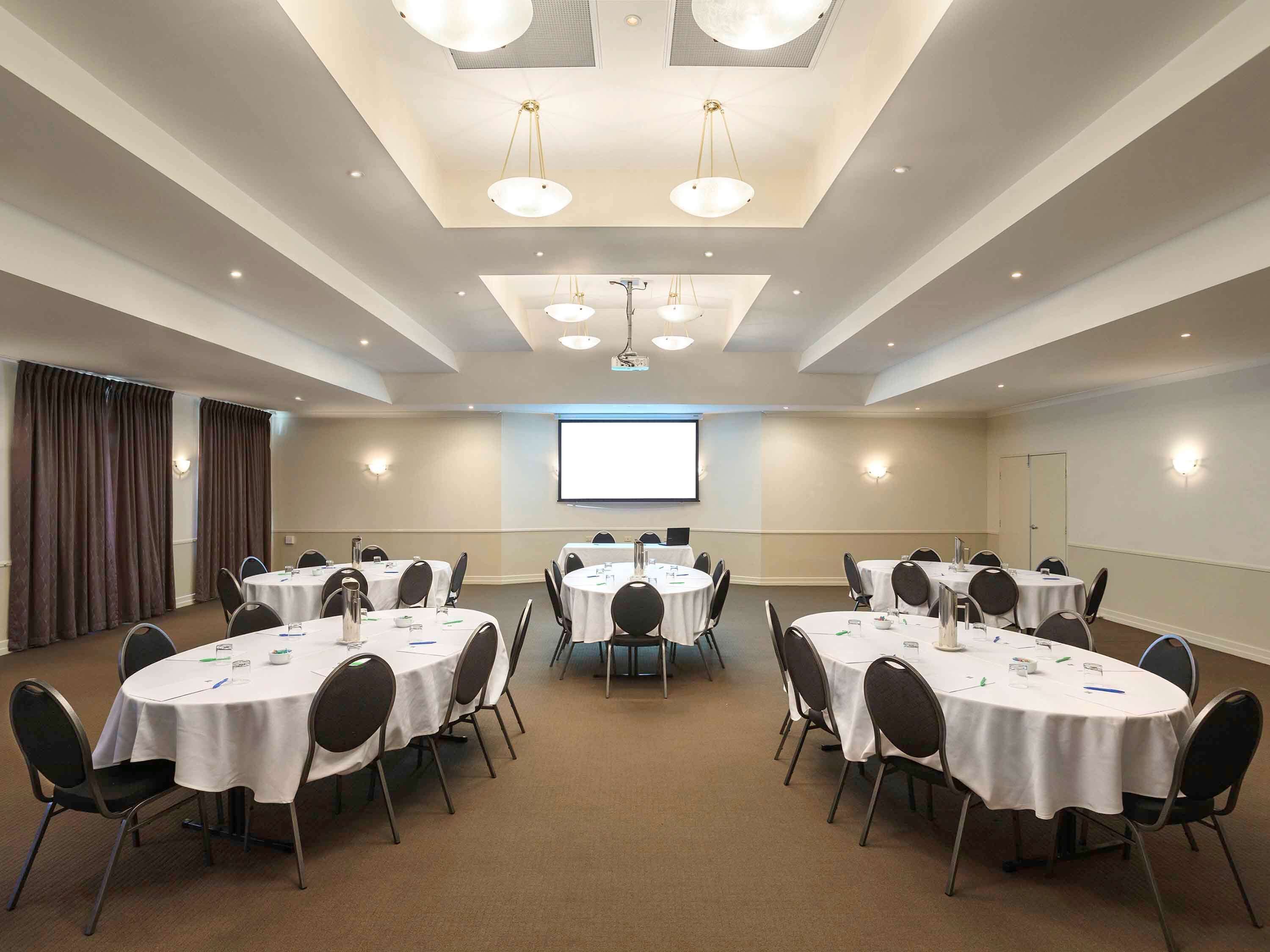 A conference room with multiple tables and chairs, a projector screen, and ceiling lights.
