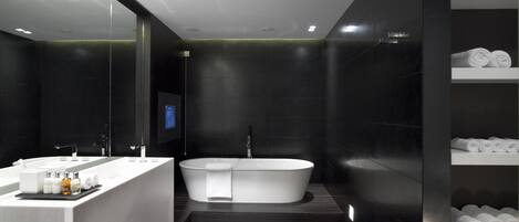 A modern bathroom with a large bathtub, a vanity with a mirror, and shelves with towels.