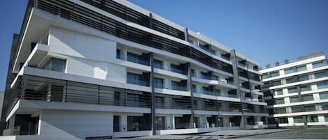 A multi-story modern building with a flat roof, large windows, and a stone-paved ground.