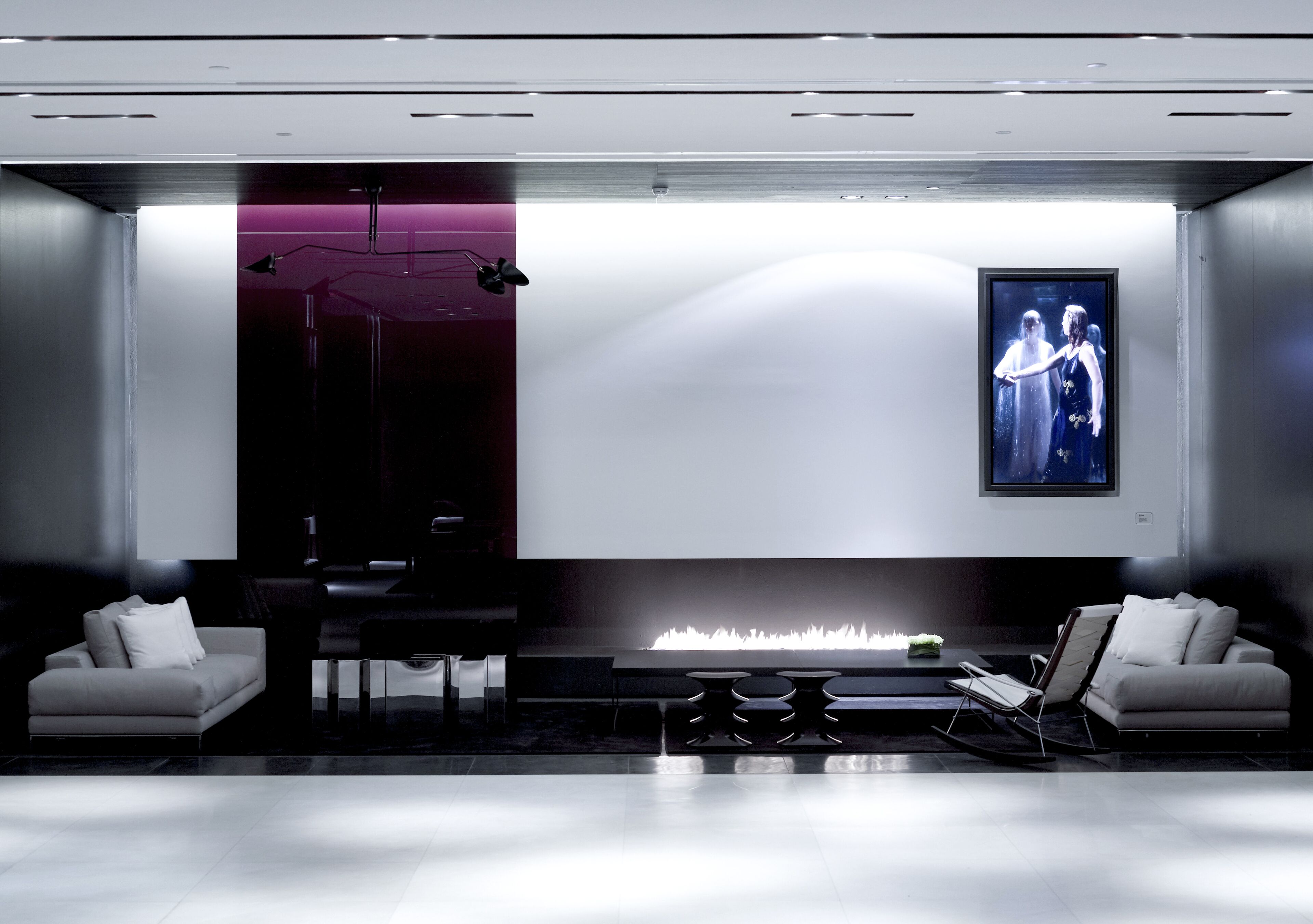 A modern, minimalist room with a large flat-screen TV, a fireplace, and two sofas.