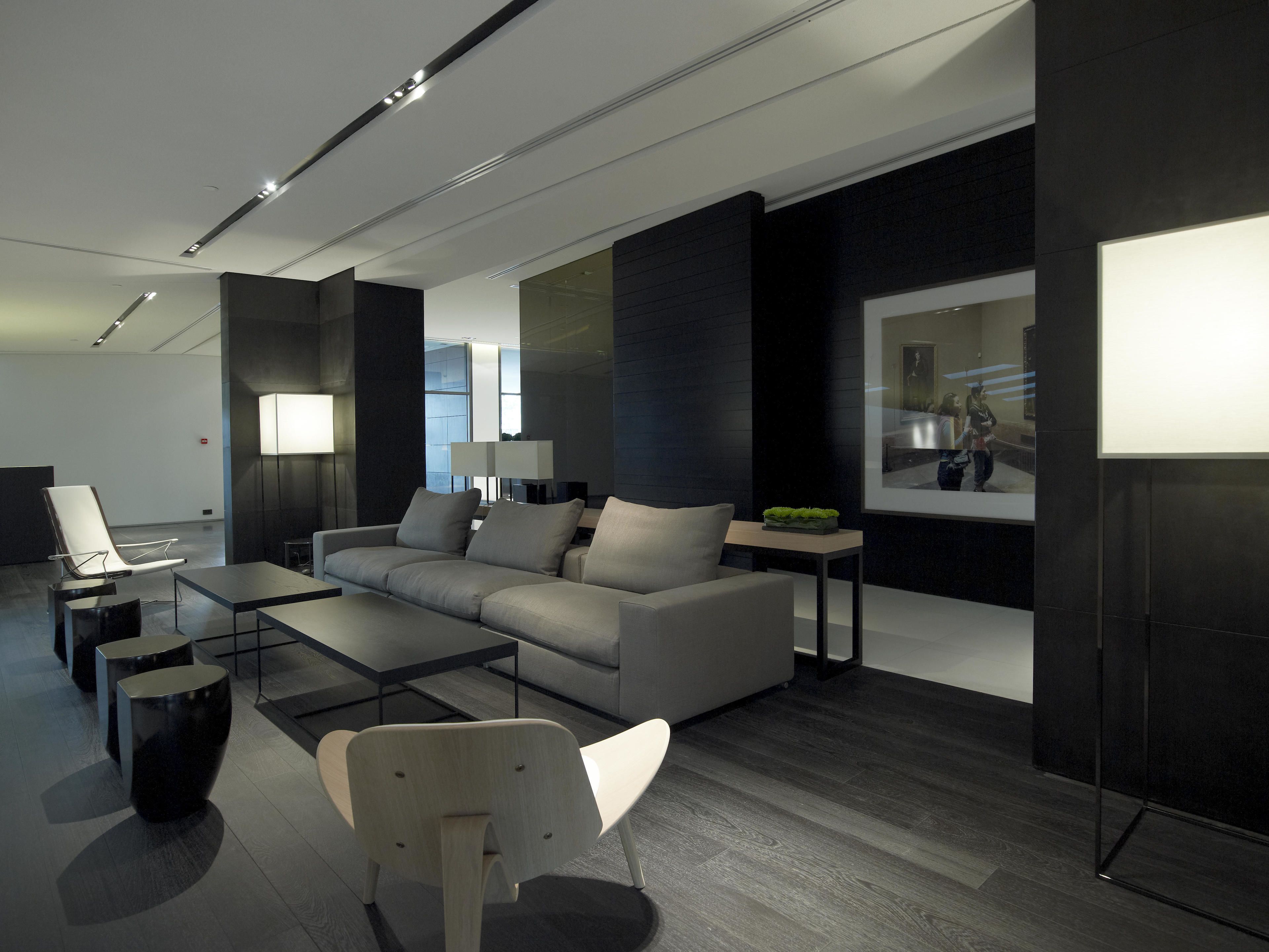 Un salón moderno y bien iluminado con sofá, mesa de centro y sillas. Hay una lámpara, una mesita con una planta y un cuadro en la pared.