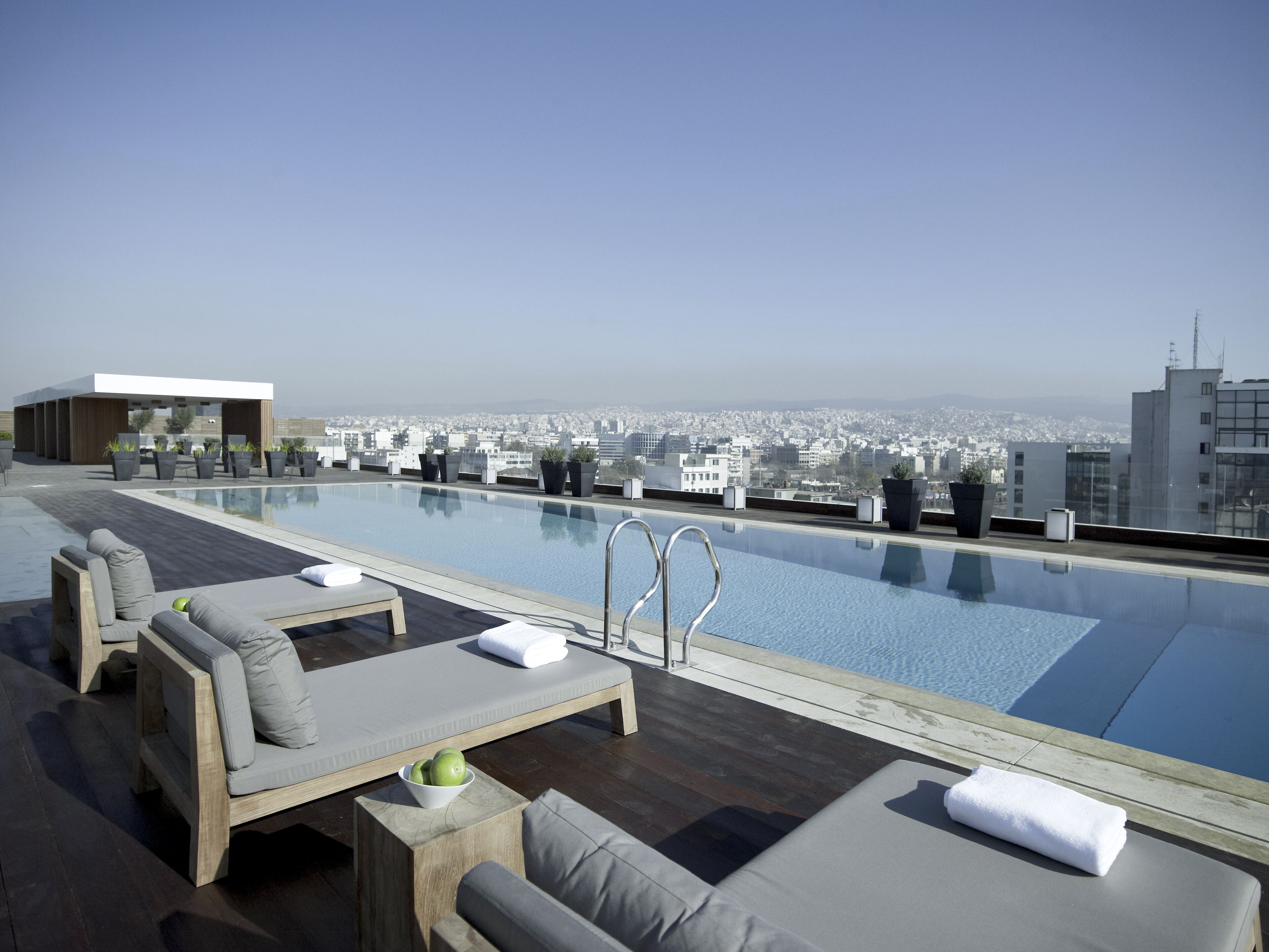 Area piscina sul tetto con poltronne relax e vista sulla città.