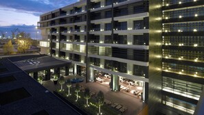 Un hôtel à plusieurs étages au design moderne, doté de balcons et d’un espace sur le toit aménagé avec des sièges extérieurs.