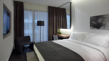 A hotel room with a large bed, a desk with a chair, a TV, and a painting on the wall.