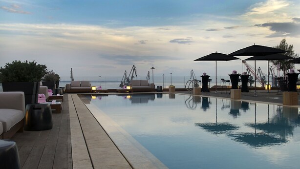 Un espace aménagé au bord de la piscine, avec des chaises longues et des parasols, une vue dégagée sur la mer et une ambiance paisible.