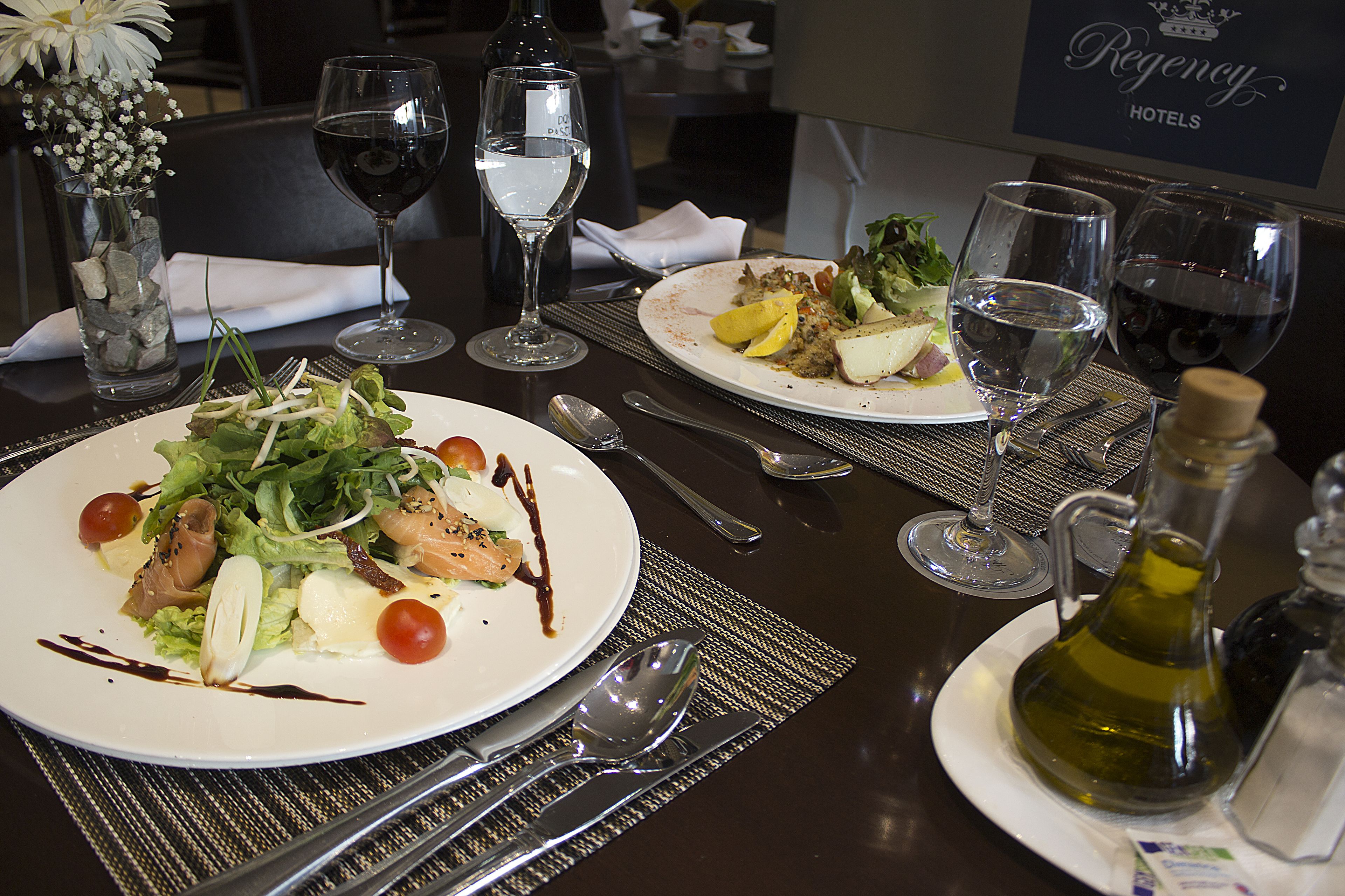 A dining table with plates of food, wine glasses, and a bottle of olive oil.