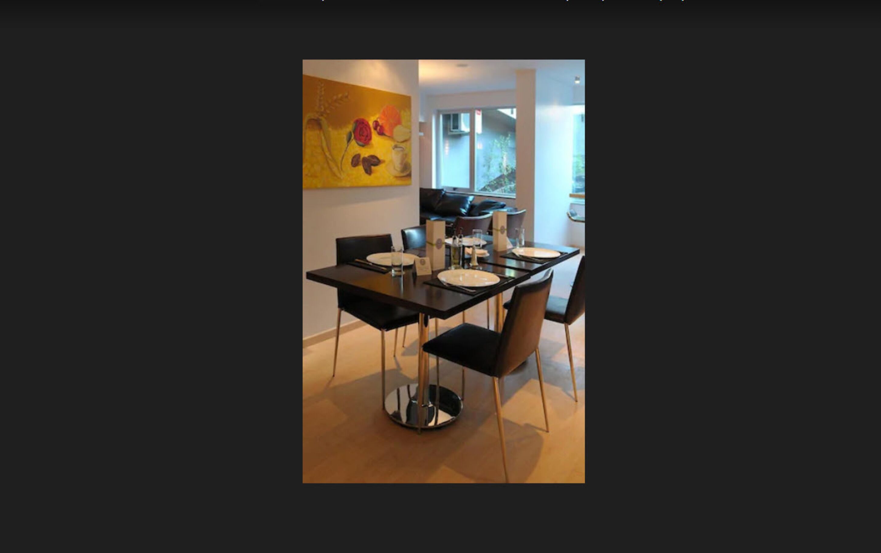 Un área de comedor moderna con una mesa y sillas negras, un cuadro amarillo en la pared y vistas al exterior a través de la ventana.