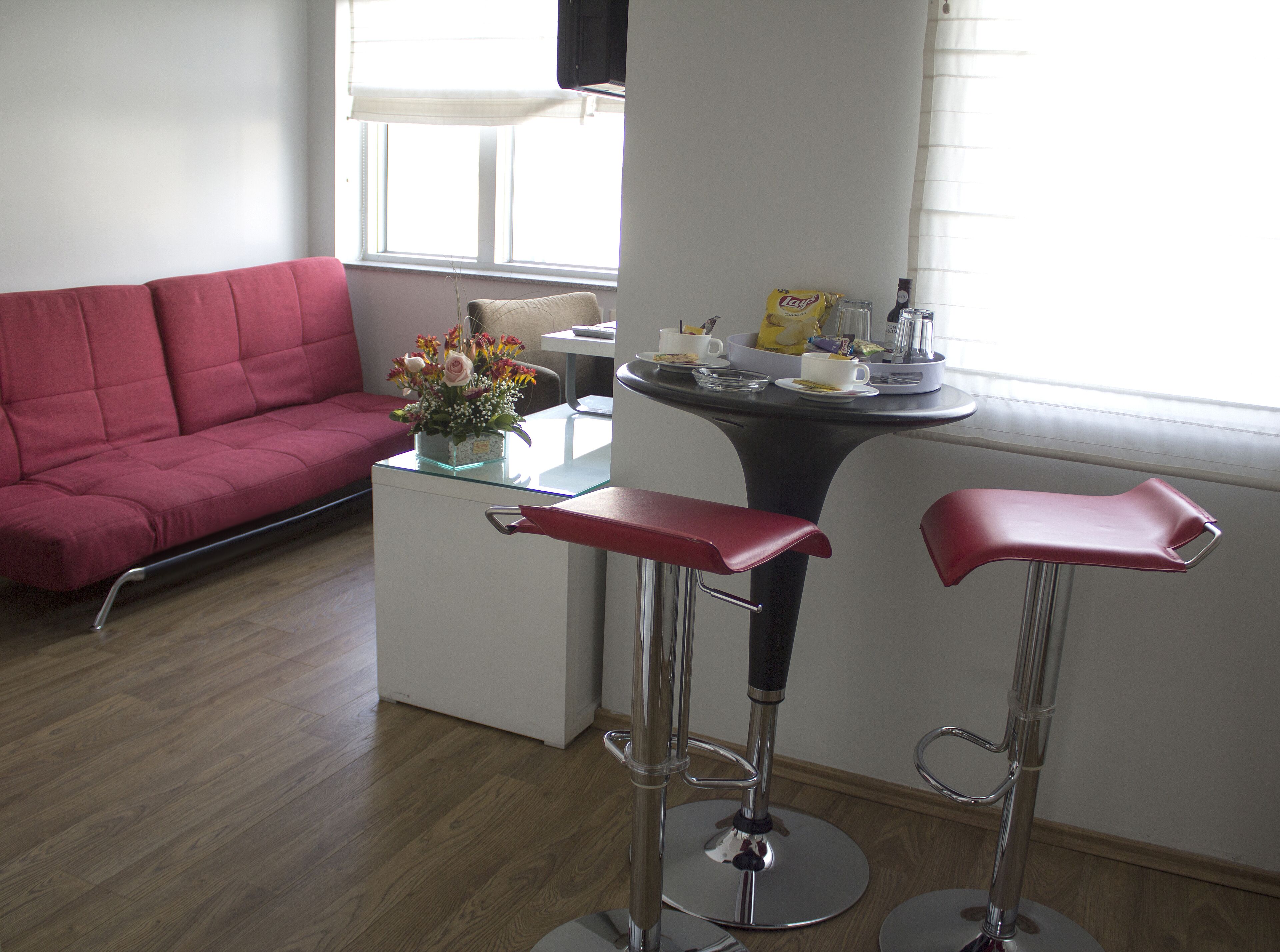Una sala moderna con un sofá rojo, una mesa de centro de vidrio y dos taburetes de bar.