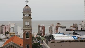 A cityscape with a prominent tower featuring a dome and cross, surrounded by modern buildings and a body of water in the background.