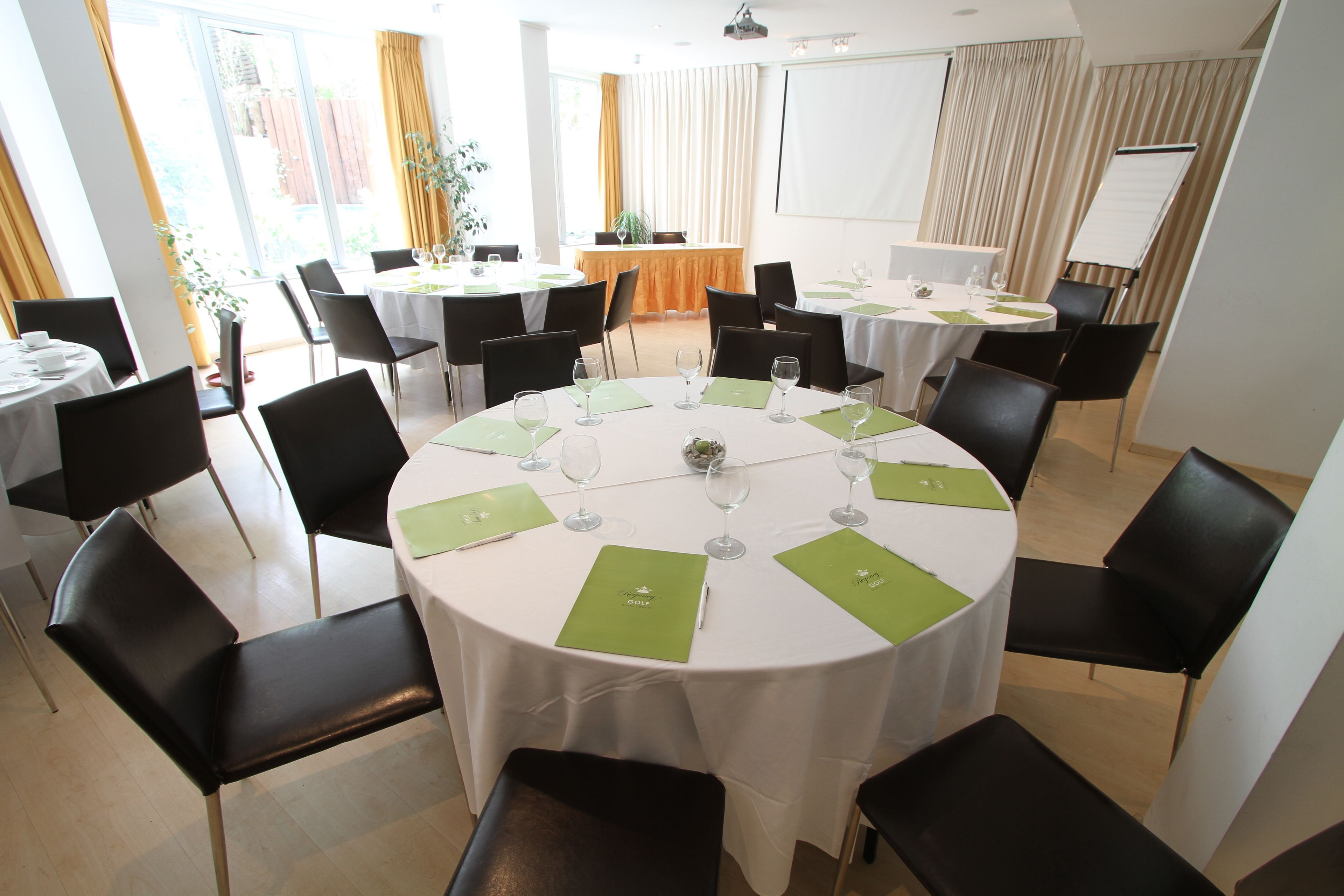 A conference room with round tables, black chairs, and green placemats.