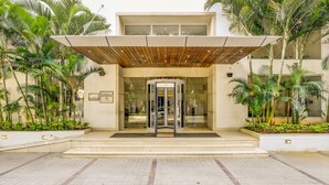 A modern building entrance with a revolving door, surrounded by palm trees and a tiled walkway. - Lemon Tree Hotel, Electronics City - Bengaluru (Bengaluru)