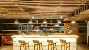 A bar area with a wooden ceiling, multiple shelves with bottles, and three bar stools. - Lemon Tree Hotel, Electronics City - Bengaluru (Bengaluru)