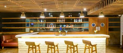 A bar area with a wooden ceiling, multiple shelves with bottles, and three bar stools.