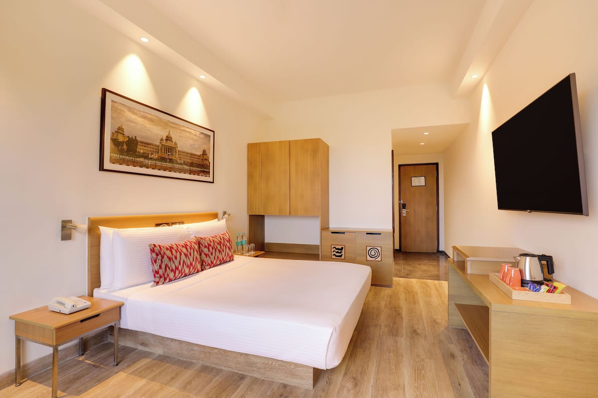 Une chambre d’hôtel avec un lit, une table de chevet, une télévision et un tableau au mur.