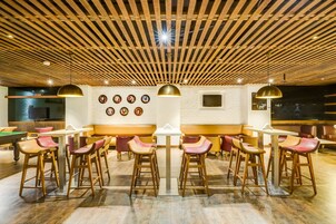 A modern bar area with wooden ceiling beams, bar stools, and a pool table.