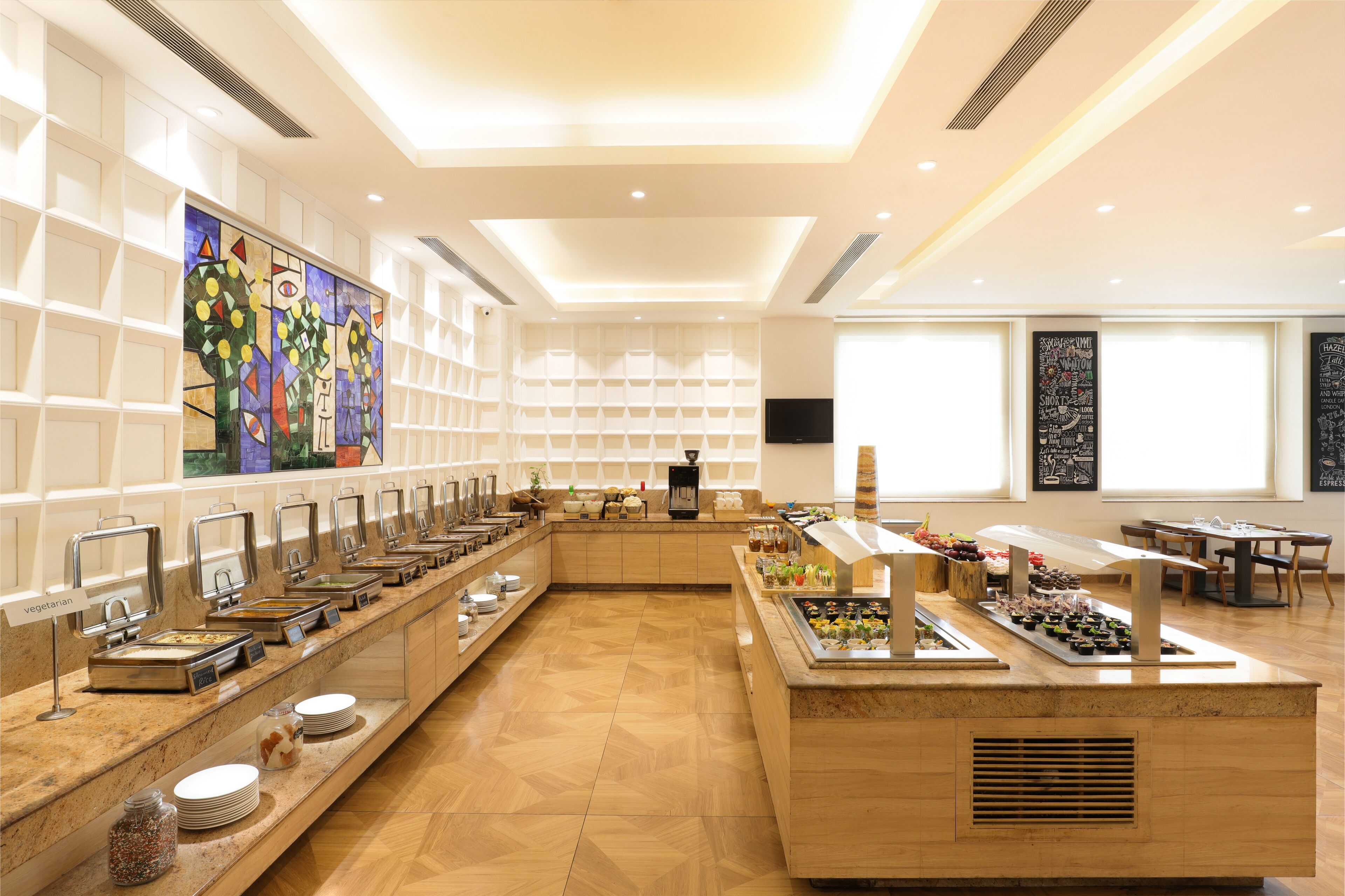 A buffet area with multiple food stations, a large painting on the wall, and a television screen.