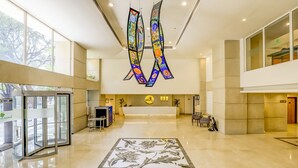 A spacious lobby with a reception desk, a glass door entrance, and a large floral patterned floor. - Lemon Tree Hotel, Electronics City - Bengaluru (Bengaluru)