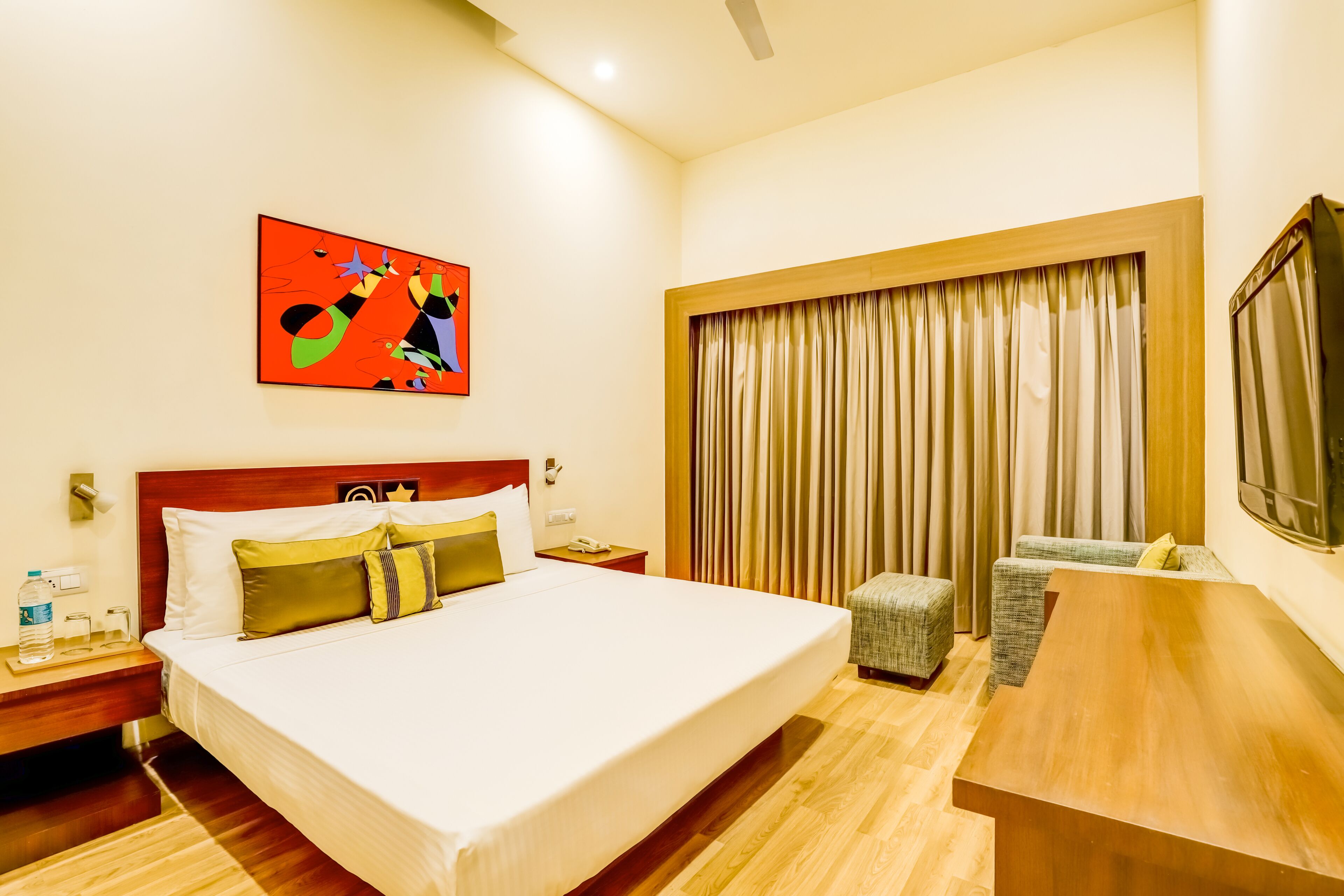 A hotel room with a large bed, a desk, a chair, a television, and a window with curtains.
