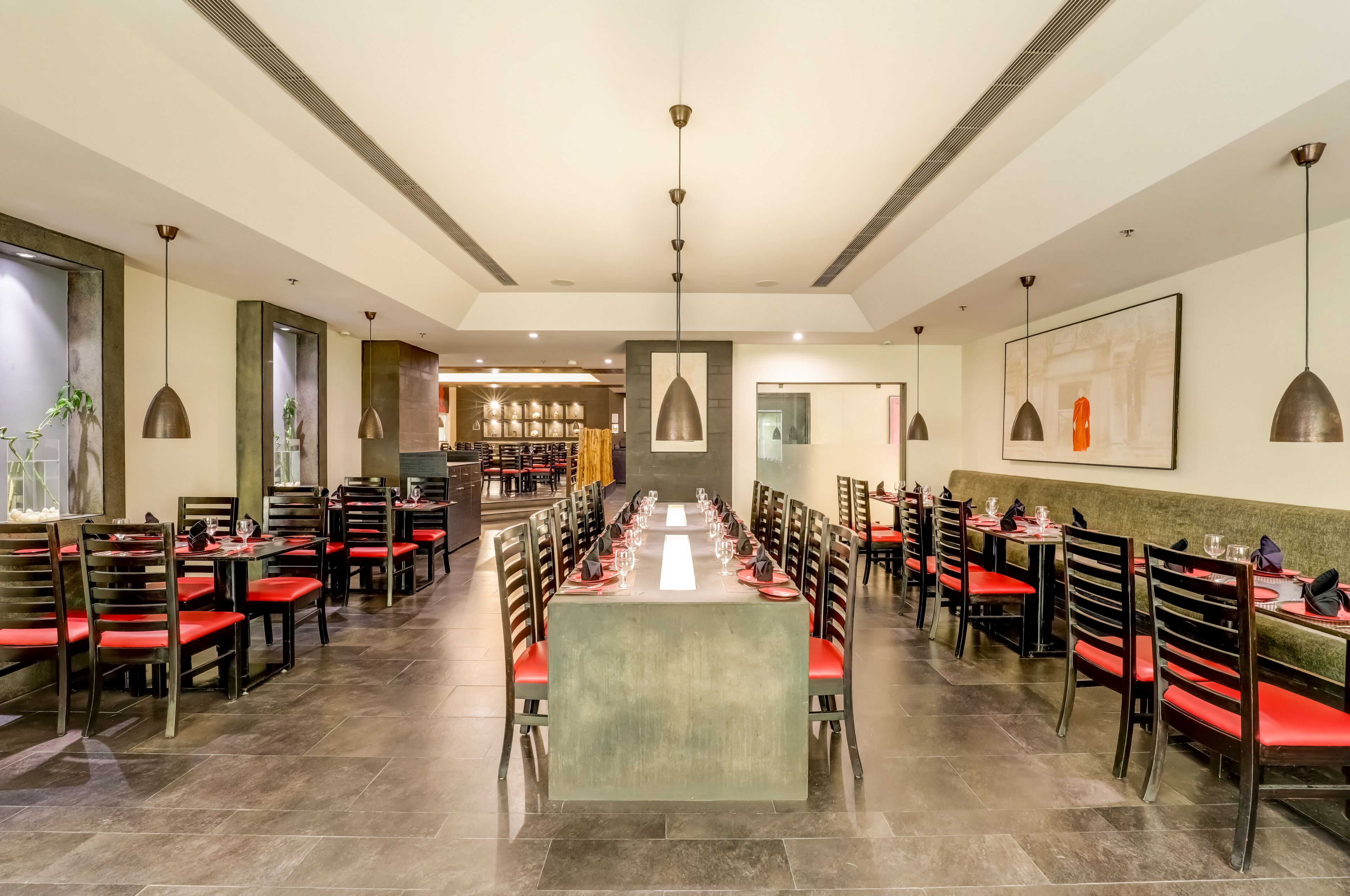 A spacious dining area with long tables and red chairs, featuring pendant lighting and a modern interior design.