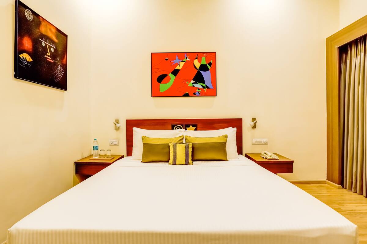 Une chambre d’hôtel avec un grand lit, deux tables de chevet, une commode, un tableau au mur et une fenêtre avec des rideaux.