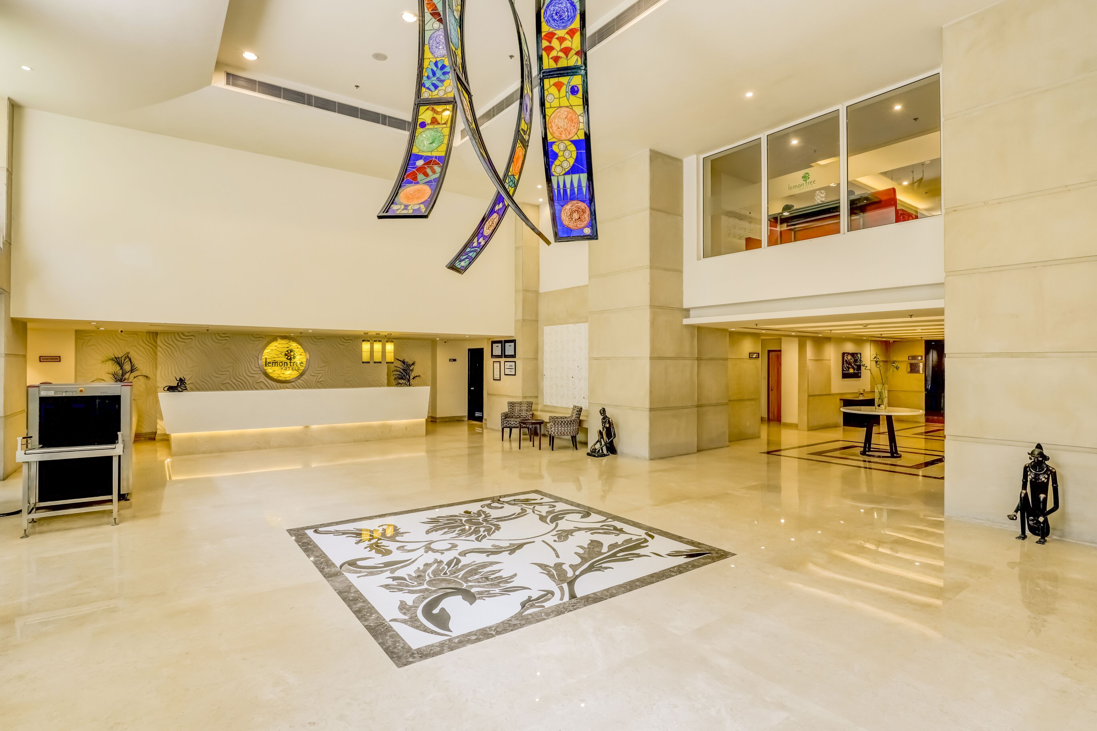 Eine geräumige Lobby mit einer Rezeption, einem großen floralen Teppich und einer hohen Decke mit Buntglasfenstern.