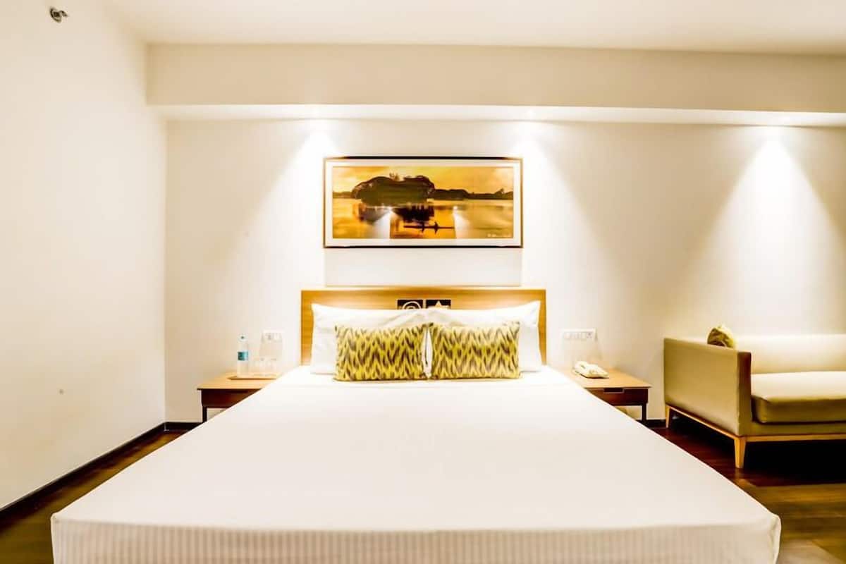 Une chambre d’hôtel avec un grand lit, une table de chevet avec une lampe, une chaise et un tableau encadré au mur.