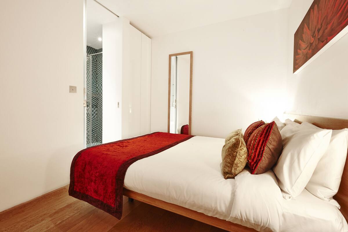 A bedroom with a wooden bed, a red throw blanket, and a mirror on the wall.