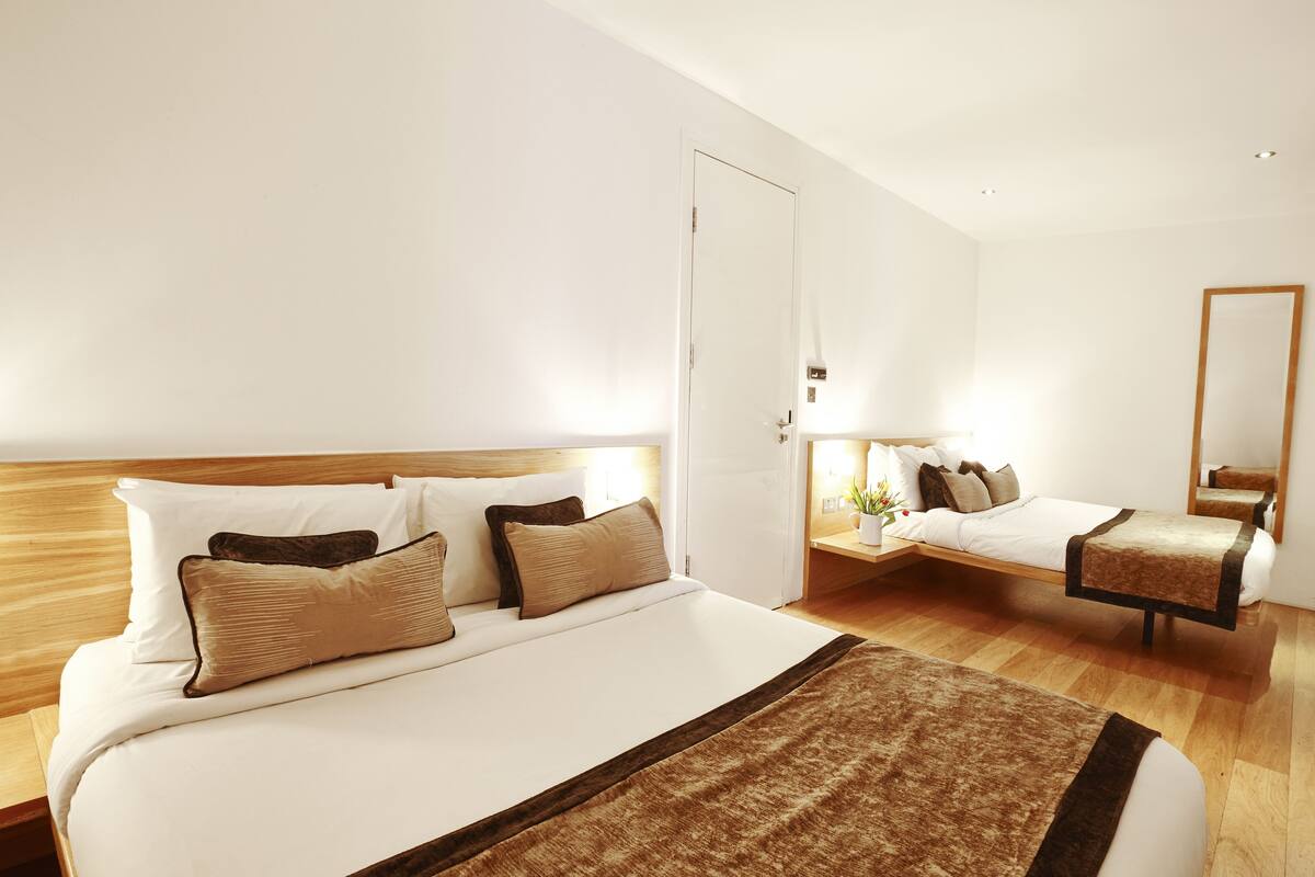 A hotel room with a large bed, a smaller bed, a bedside table, a nightstand, a mirror, and a door.