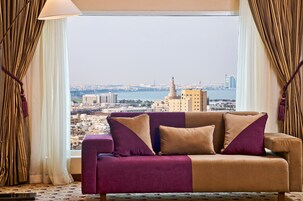 A room with a large window offering a city view, a sofa with cushions, and curtains.