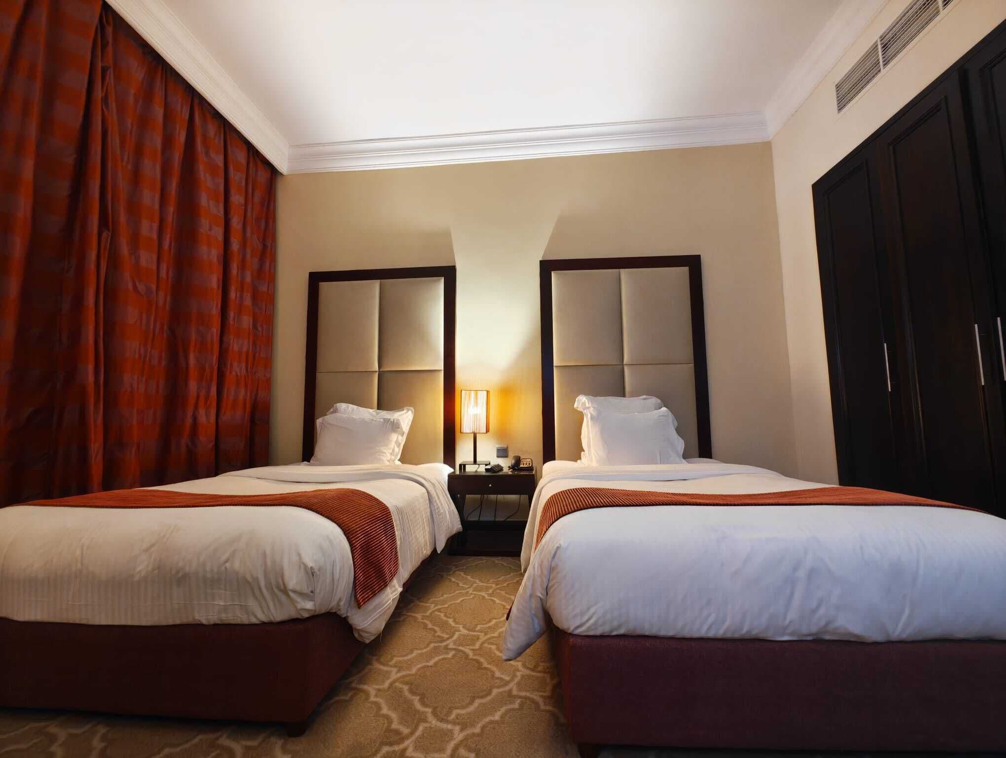 A hotel room with two beds, a nightstand with a lamp, a wardrobe, and a large mirror.