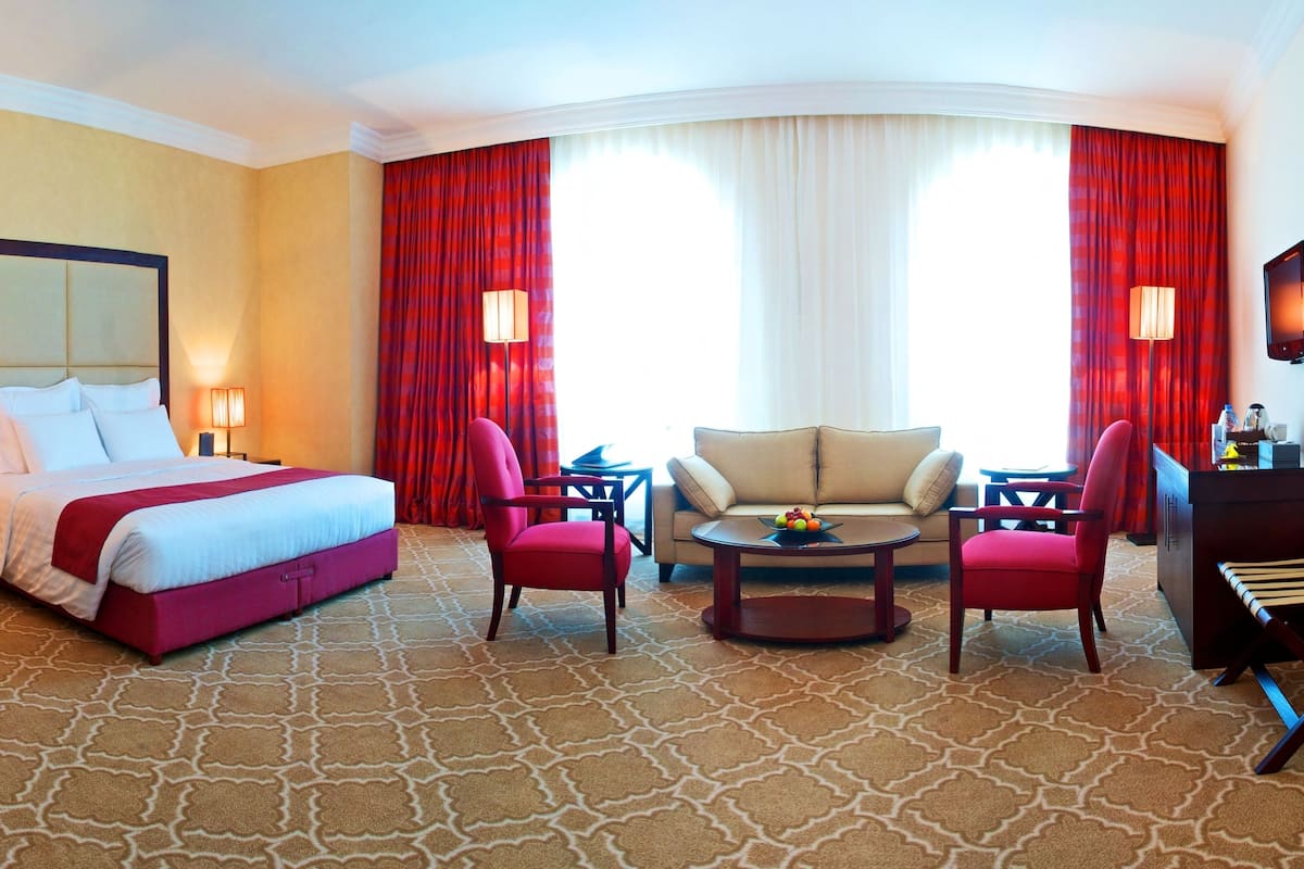 A hotel room with a large bed, two armchairs, a coffee table, a desk, and a TV.