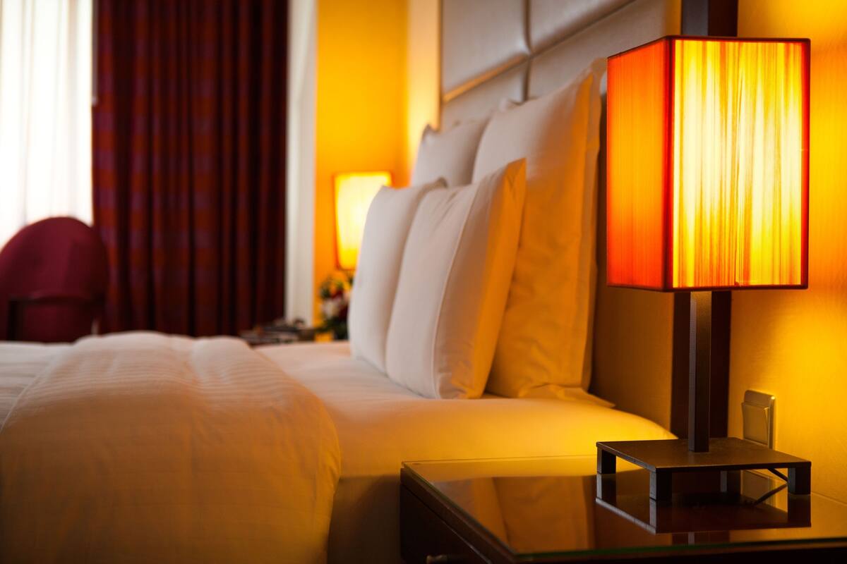 A hotel room with a bed, a nightstand, and a lamp.
