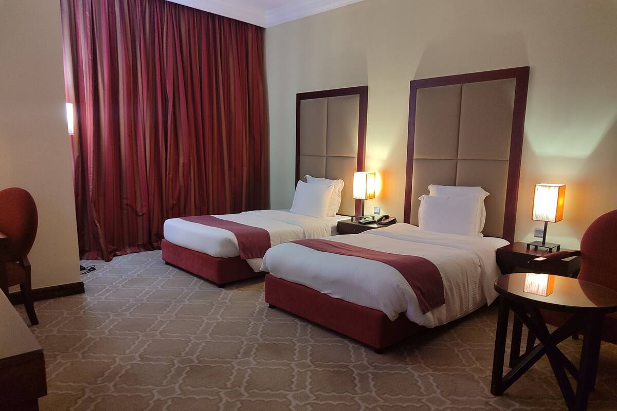 A hotel room with two beds, a desk, a chair, a lamp, and a large window with curtains.