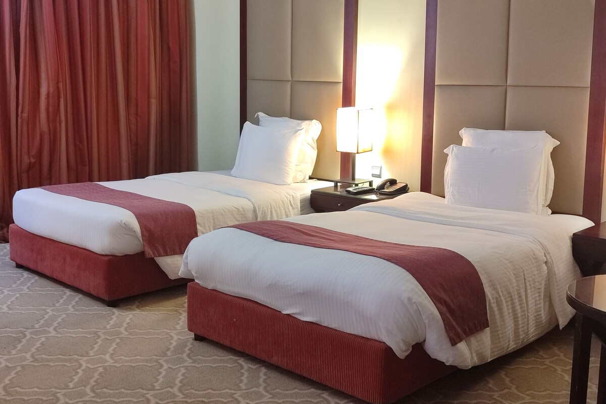 Une chambre d’hôtel avec deux lits, une table de chevet avec une lampe et un grand miroir.