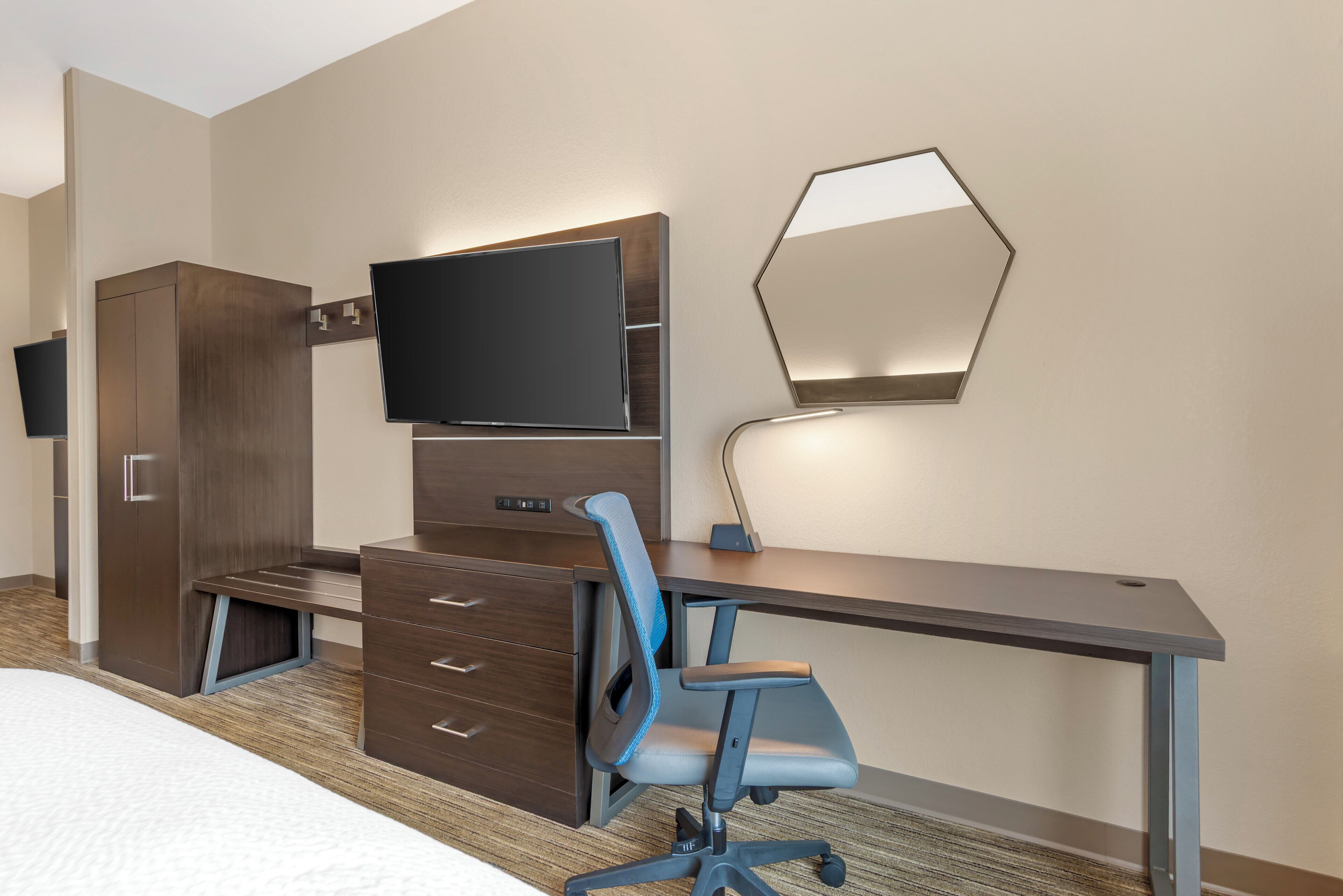 A hotel room with a bed, a desk with a chair, a TV, a wardrobe, and a mirror.