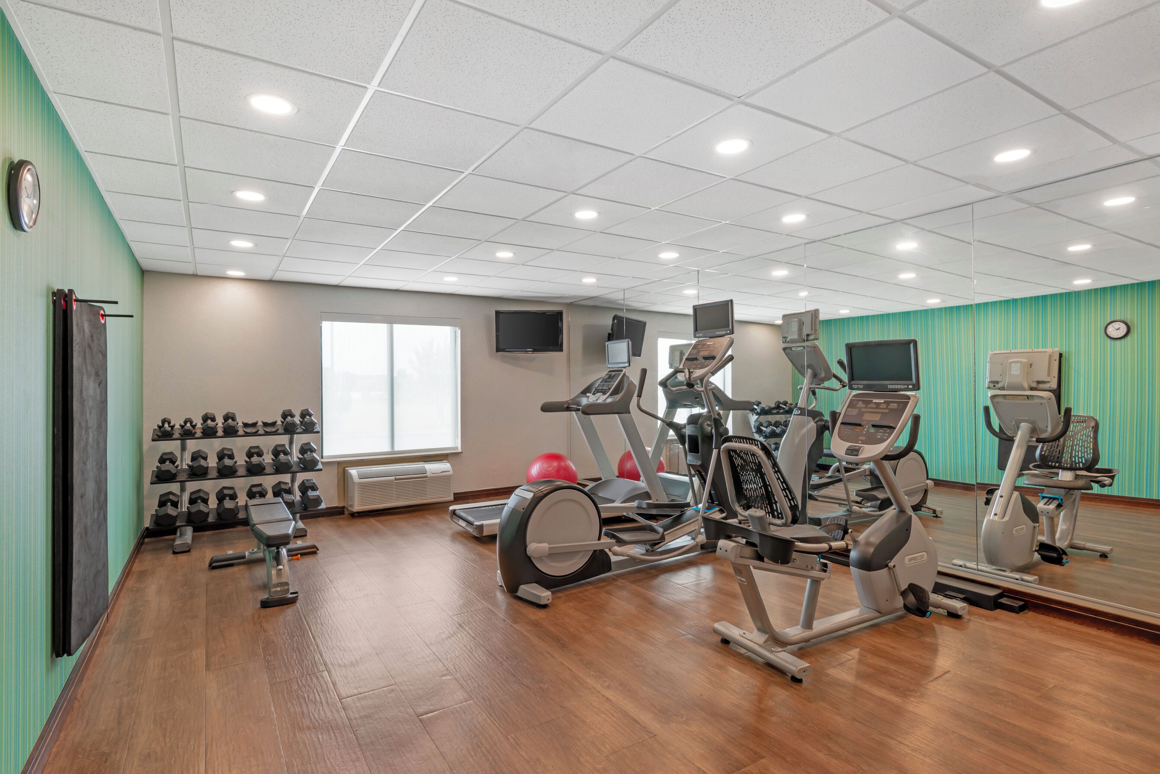 Un gimnasio con equipo de ejercicio, un espejo y un televisor montado en la pared.