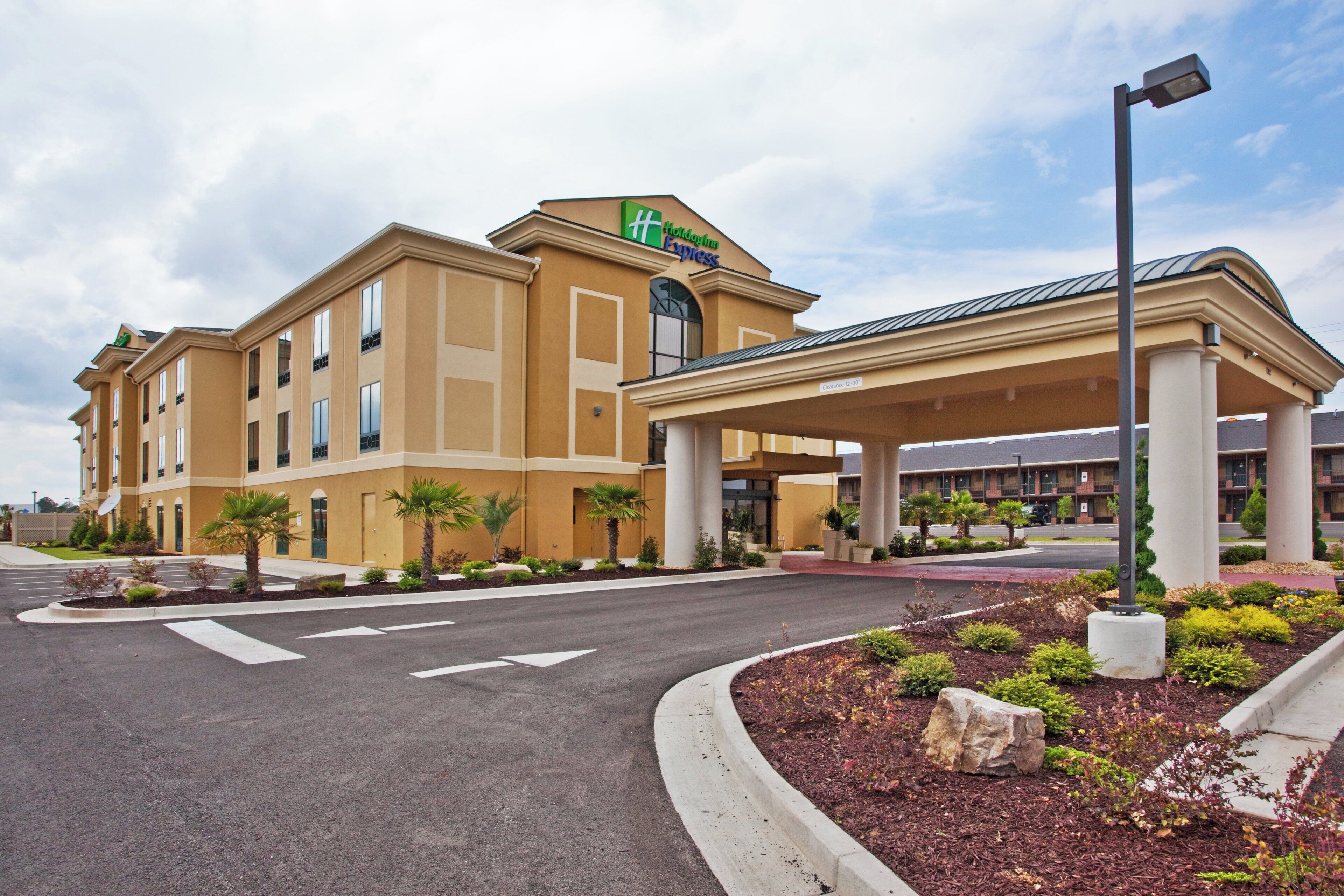 A Holiday Inn Express hotel with a covered entrance, palm trees, and a clear sky.