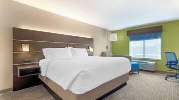 A hotel room with a large bed, bedside tables, a desk with a chair, a window with a view, and a wall-mounted lamp.