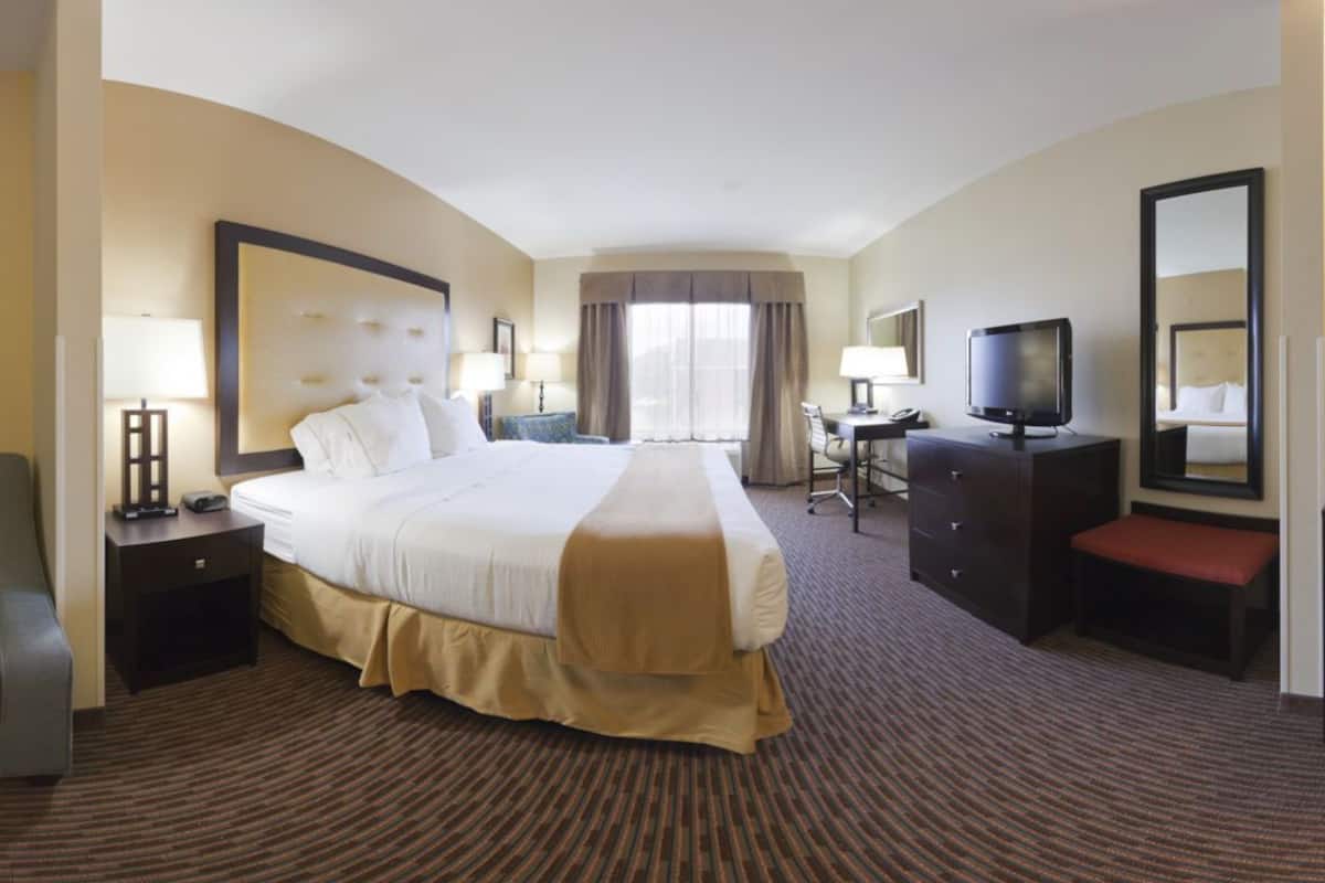 Ein Hotelzimmer mit einem großen Bett, einem Schreibtisch mit Stuhl, einem Fernseher und einem Sofa.