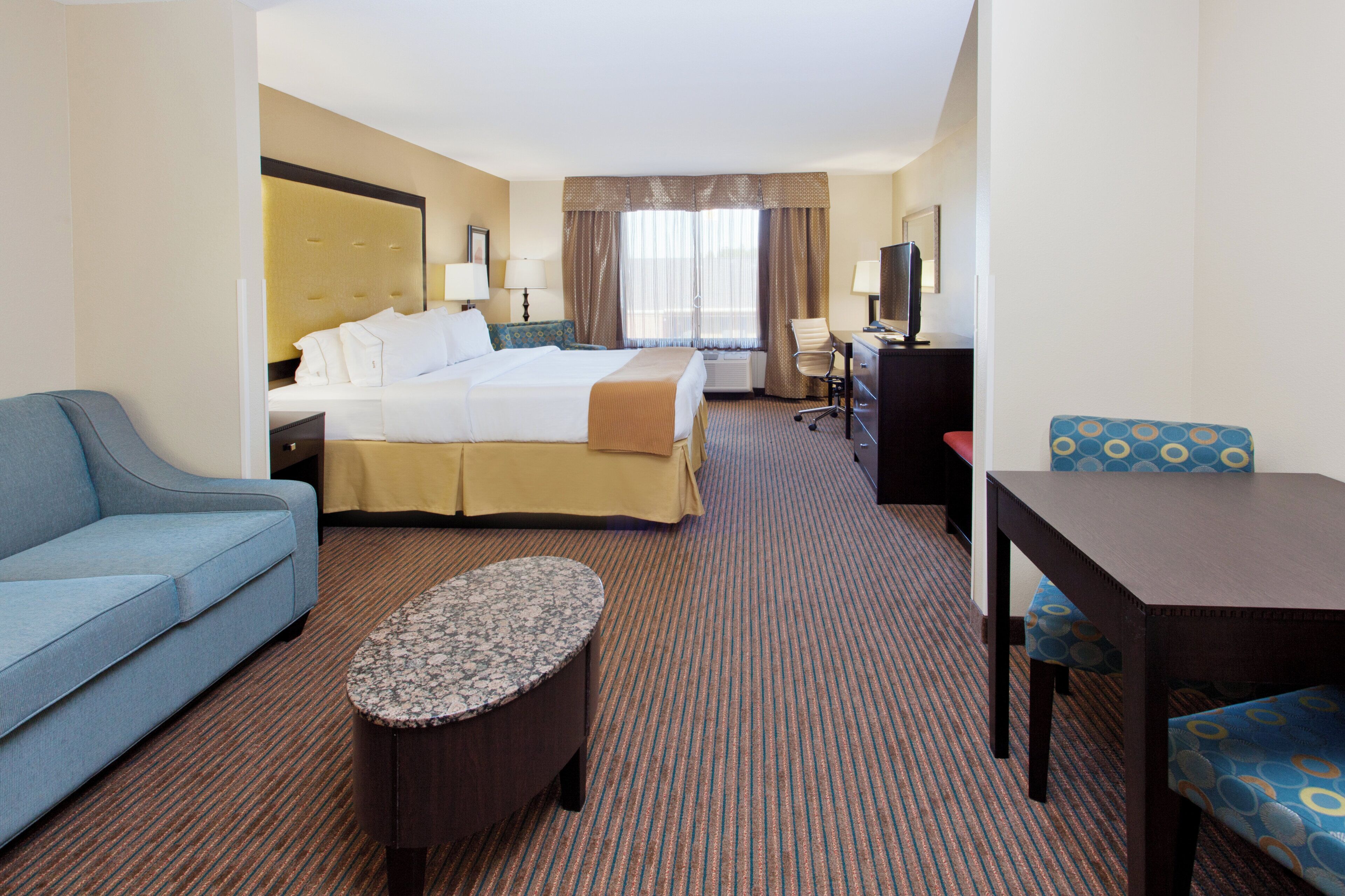 A hotel room with a bed, a desk, a chair, a sofa, and a small table.