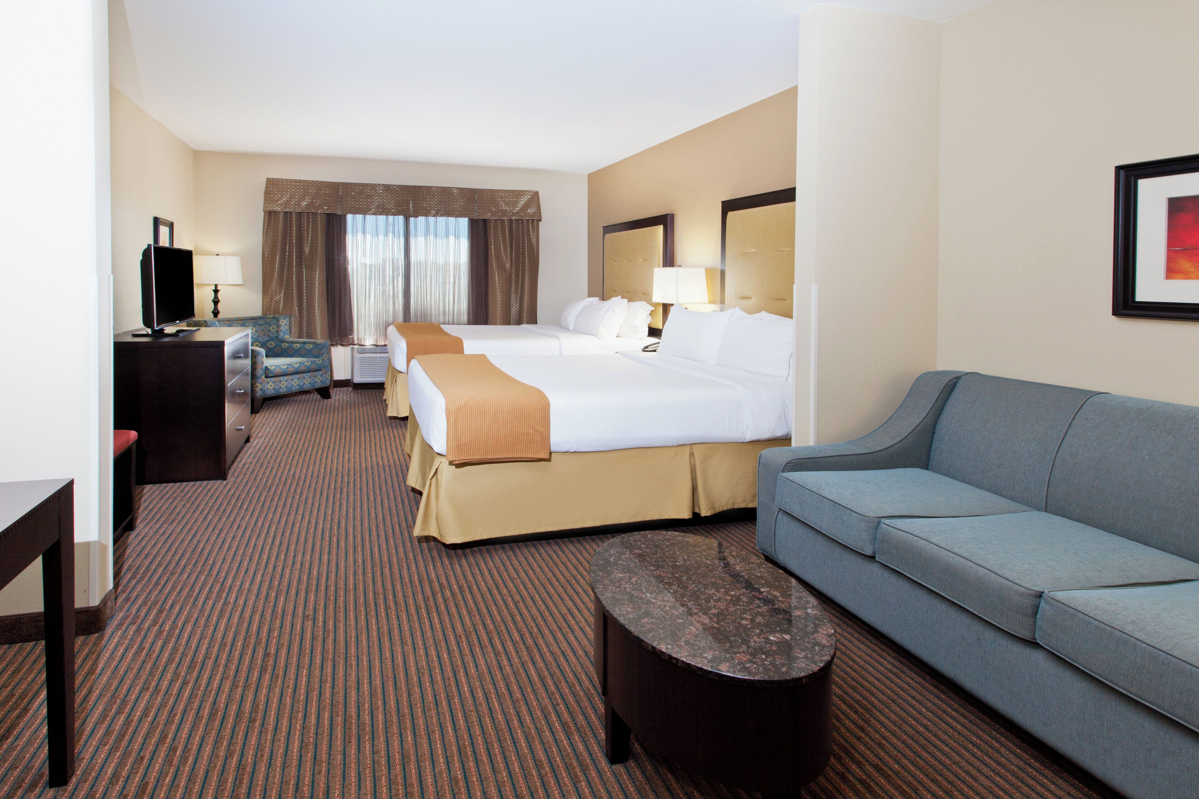 A hotel room with a large bed, a sofa, a desk with a computer, and a TV.