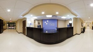 A hotel reception area with a curved black reception desk, a blue wall with a sign, and a ceiling with recessed lighting. - Holiday Inn Express Hotel & Suites CORDELE NORTH by IHG (Cordele)