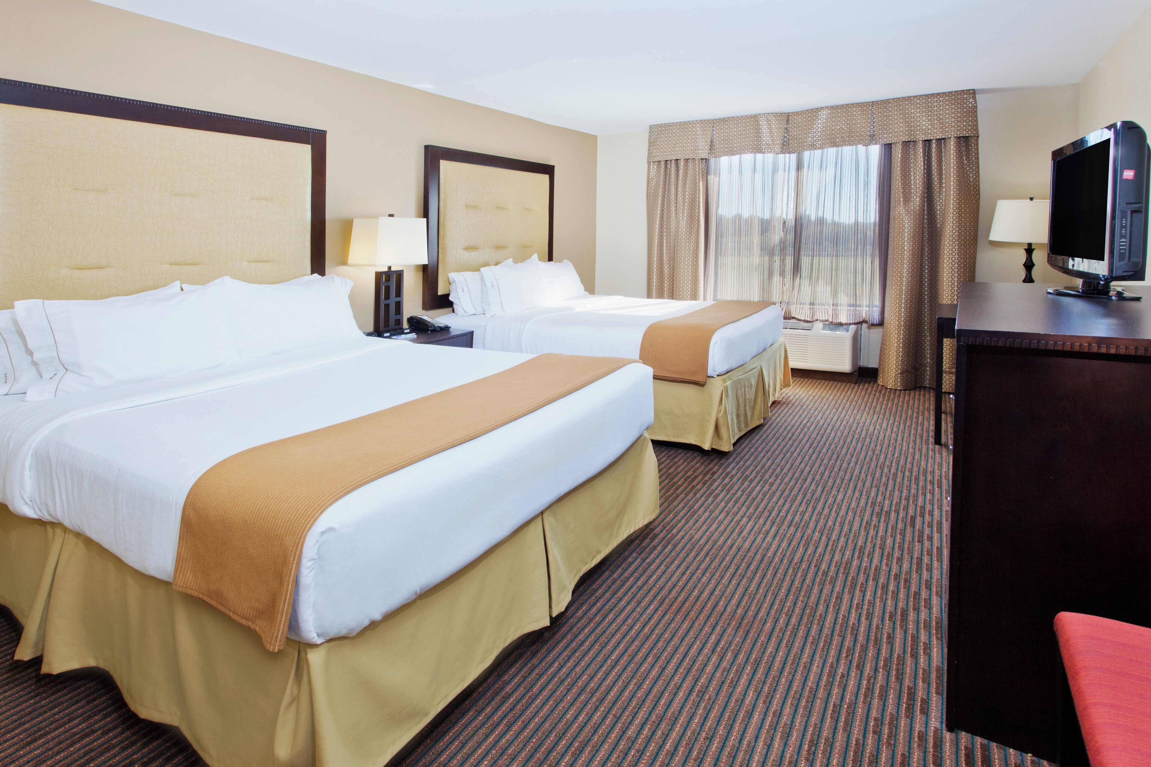 A hotel room with two beds, a desk, a television, and a window with curtains.