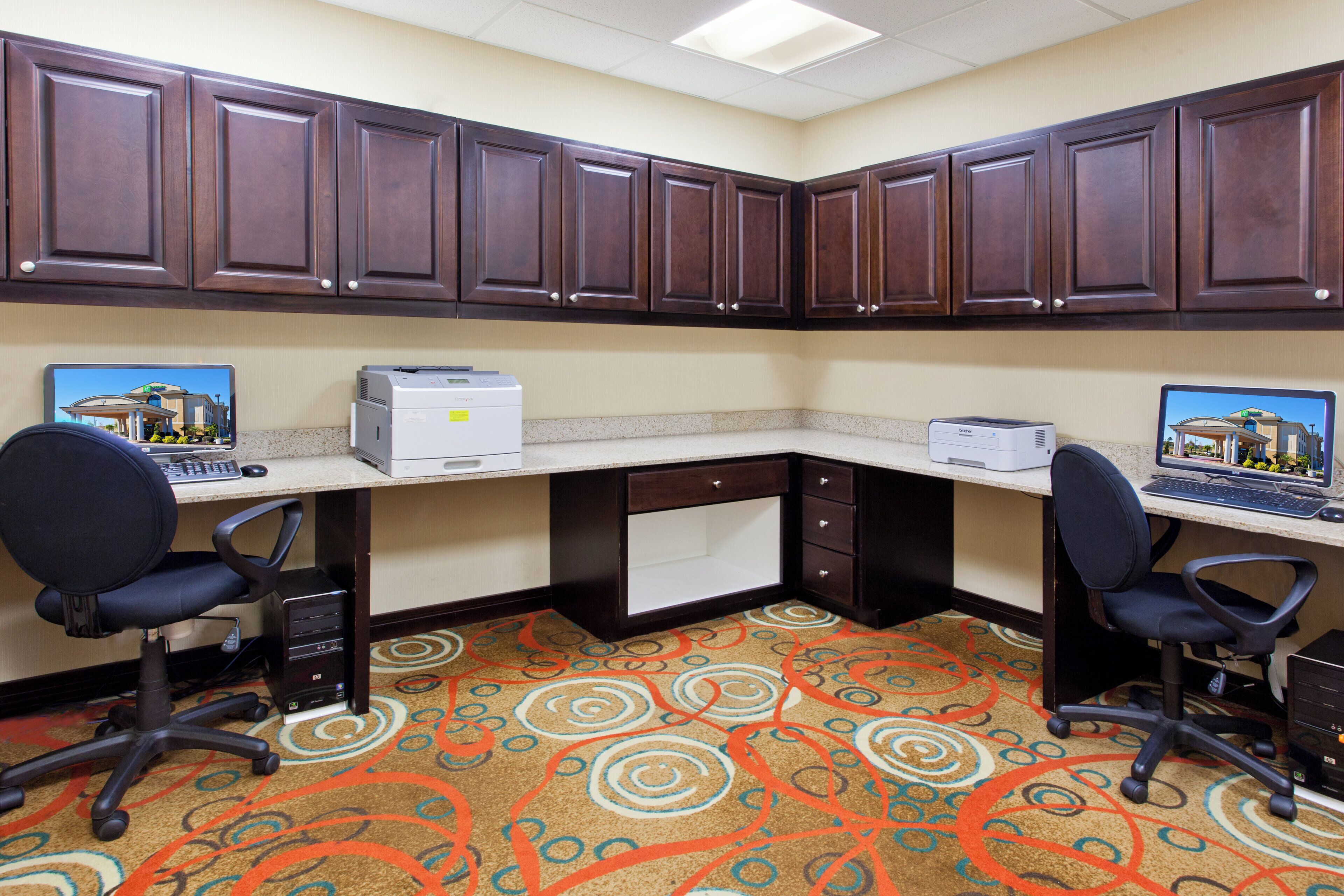 A corner office with two desks, each with a computer and printer, and a carpeted floor.