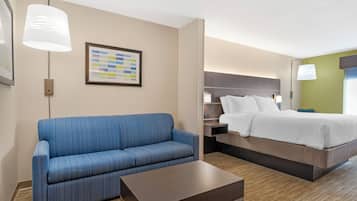 A hotel room with a blue sofa, a bed with white linens, a small table, and a wall-mounted picture.