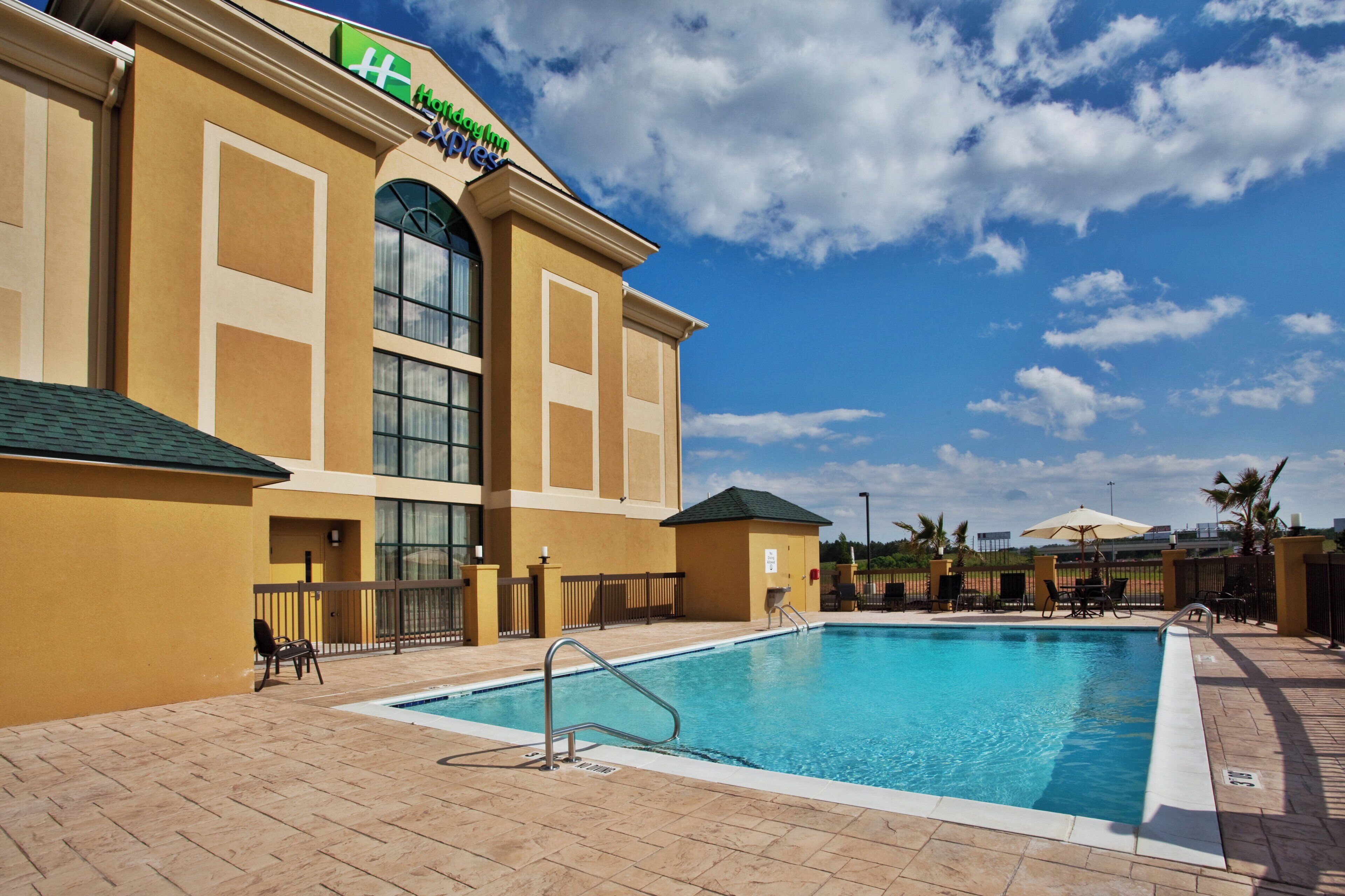 Hotel med swimmingpool, udendørs siddepladser og en klar himmel.