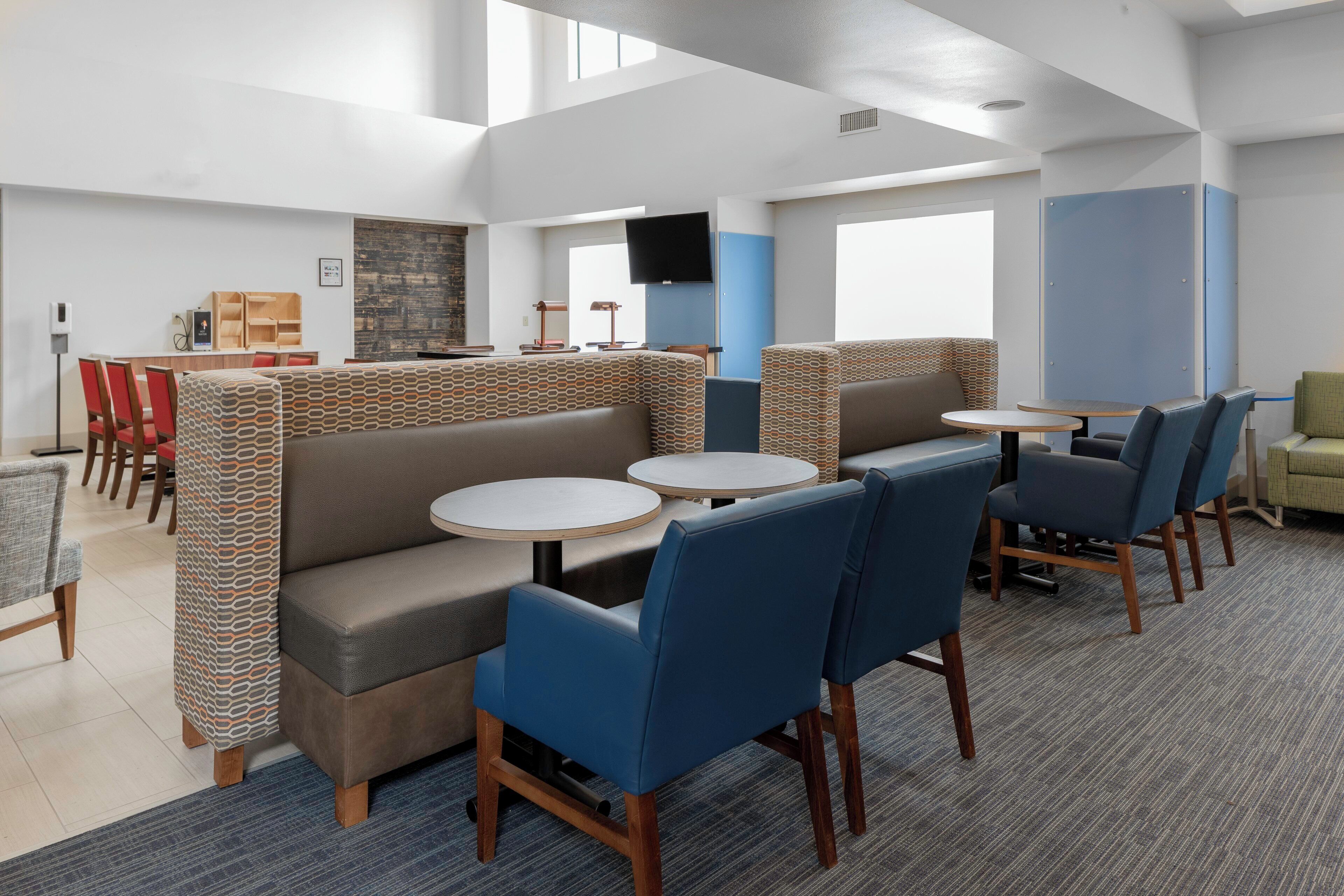 A modern hotel lobby with seating areas, a flat-screen TV, and a reception desk.